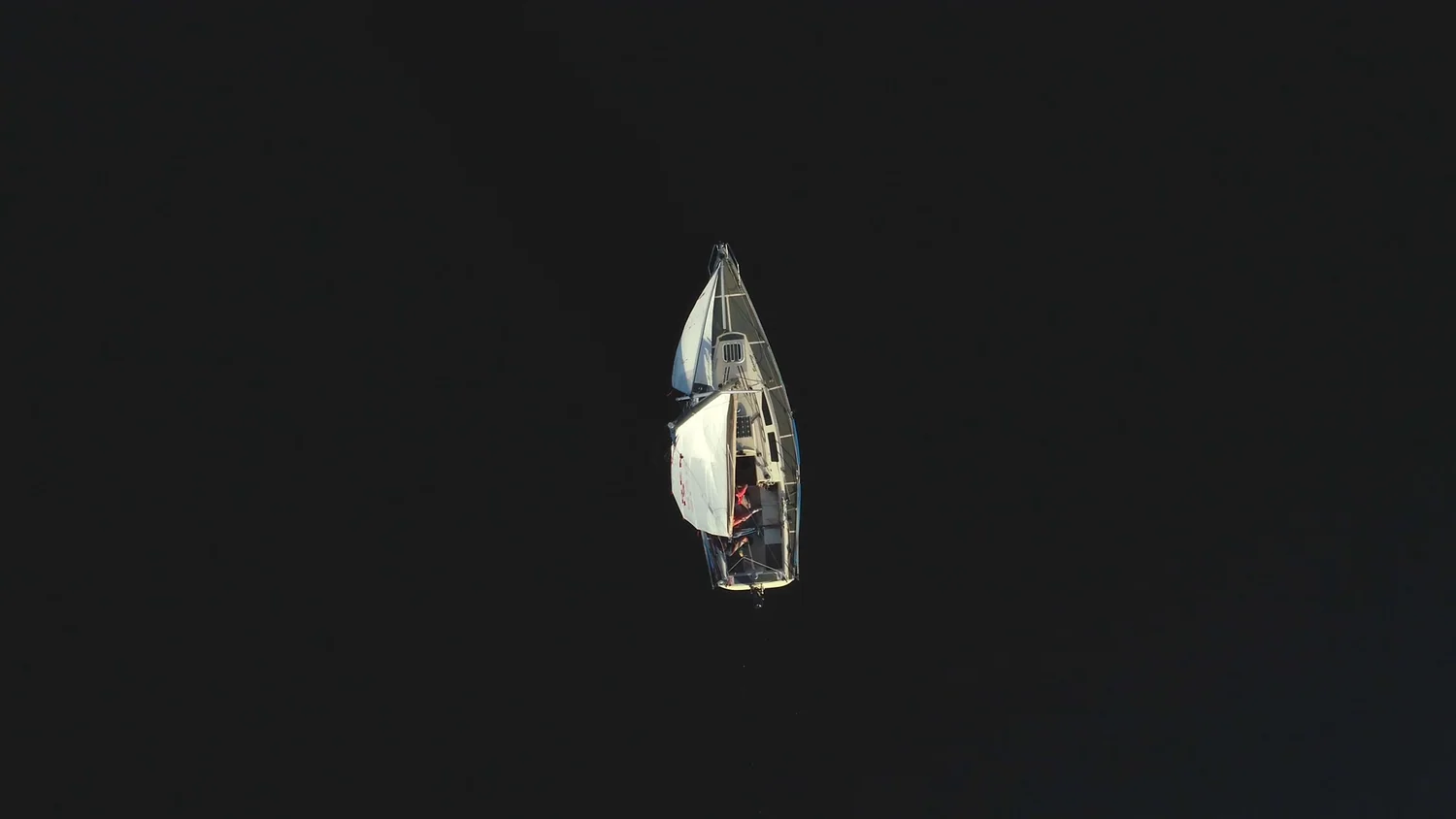 A sailing boat seen from above on dark open water