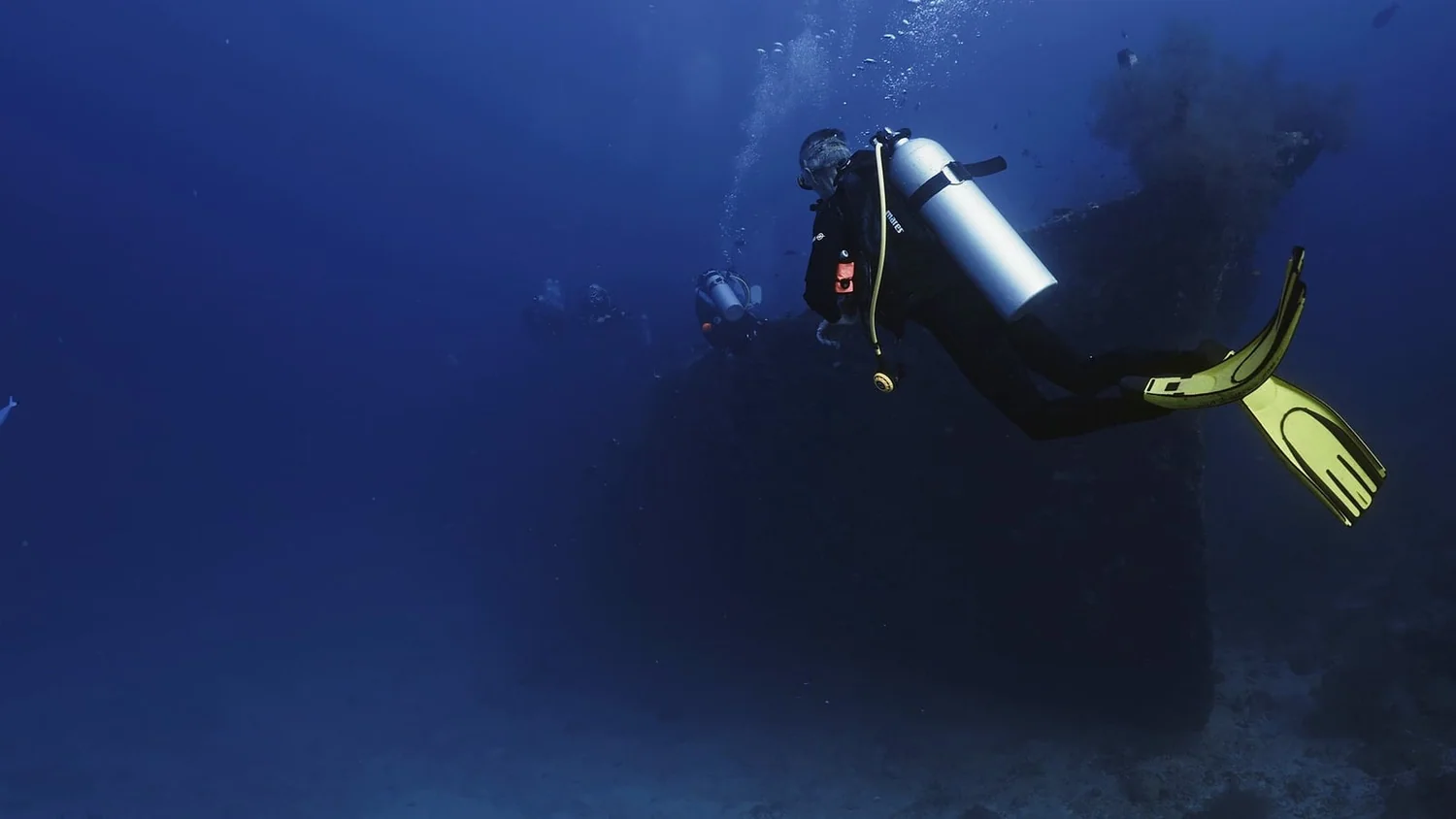 Divers descending along a wreck in deep blue water