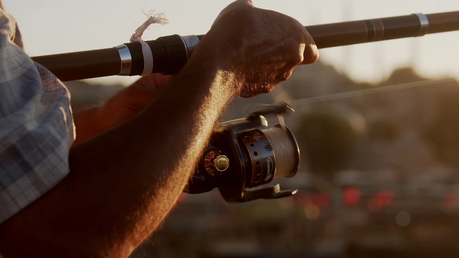 An angler holding a spinning rod, the reel's spool and bail wire visible in golden light