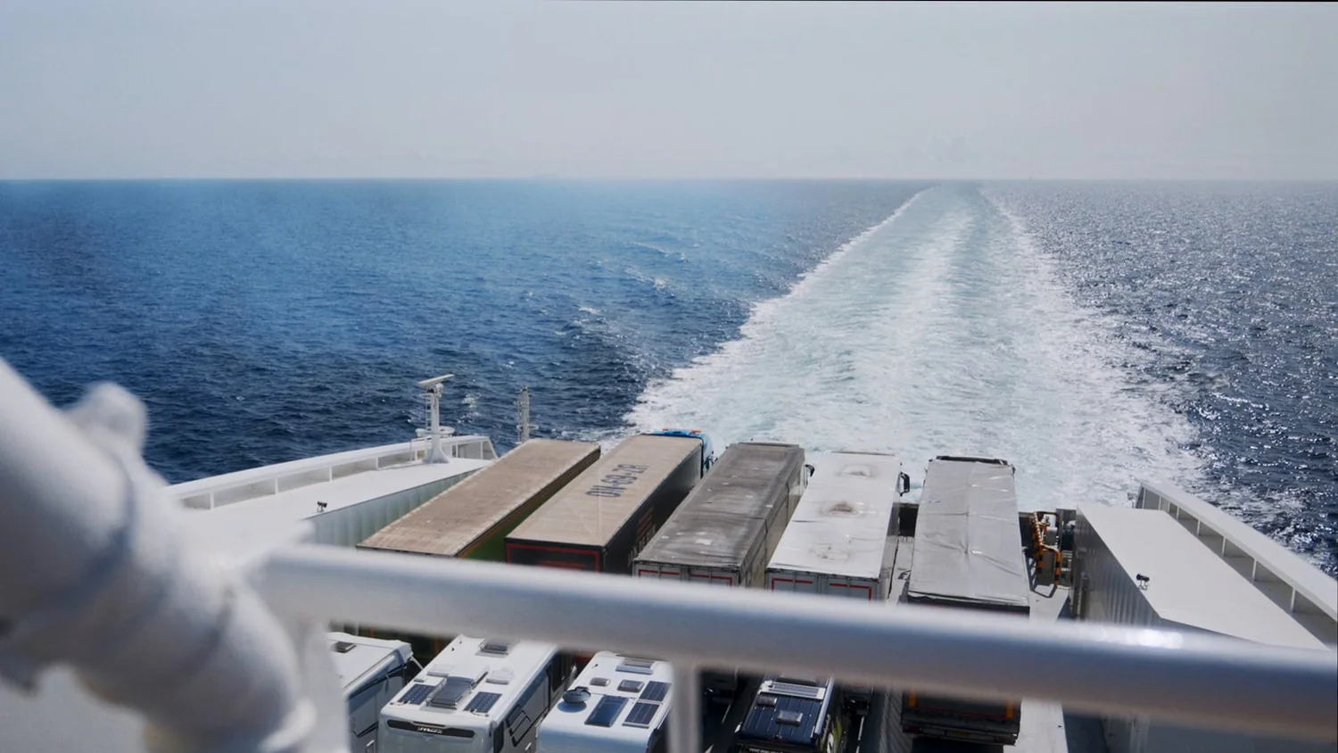 Looking astern from the upper deck of a ferry underway, wake stretching to the horizon