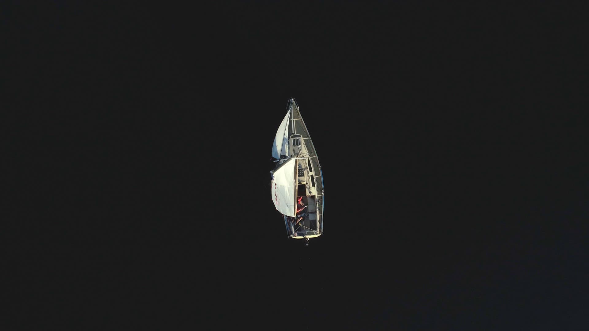 A sailing boat seen from above on dark open water