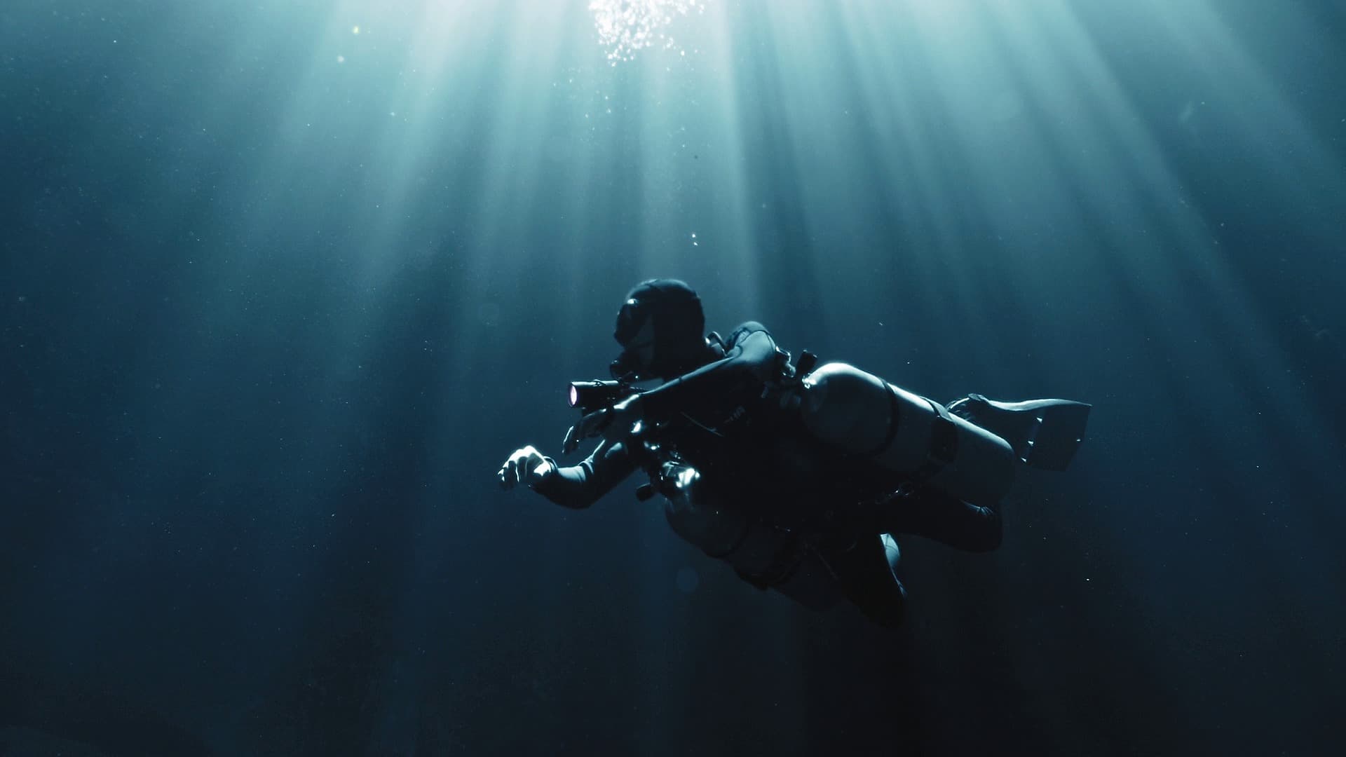 A diver in full kit with a light and camera, backlit by godrays